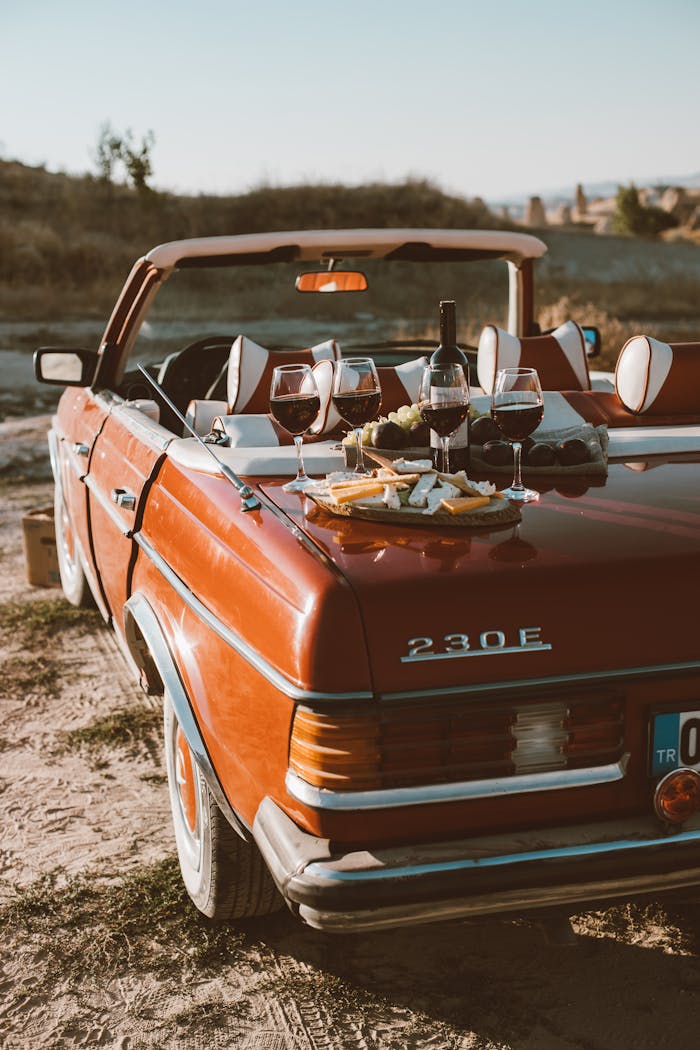 Enjoy a scenic outdoor picnic with wine and cheese on a classic red convertible.